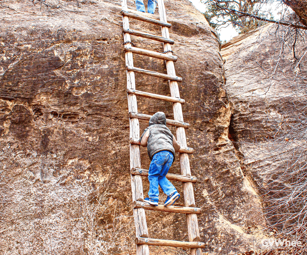 Boy climbing a woden ladder over a cliff in Utah park