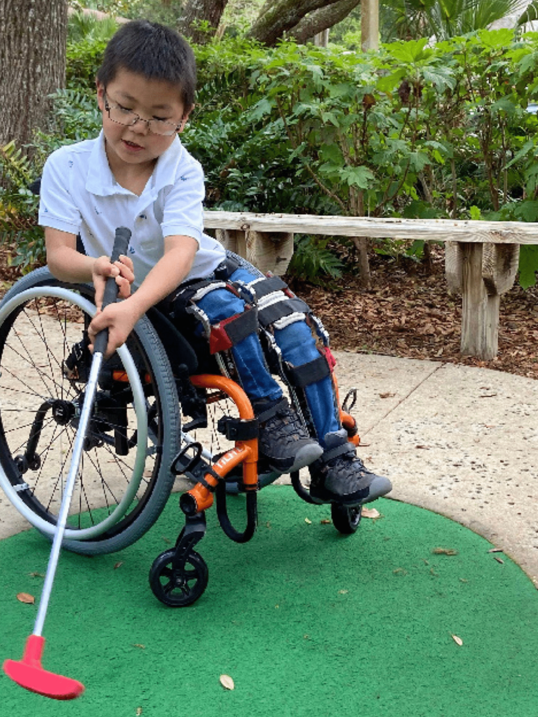 Little boy in a wheelchair playing putt putt golf