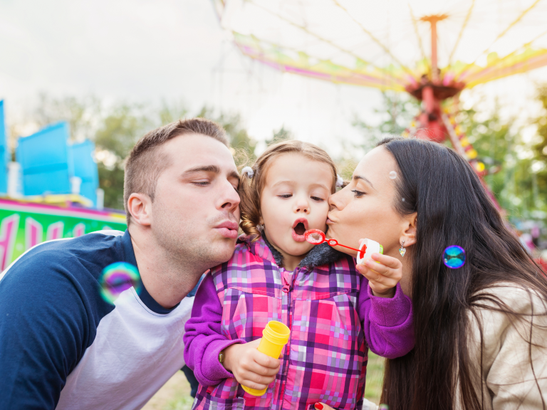 Best theme parks in the U.S cover photo with family blowing bubbles in an amusement park with attractions behind